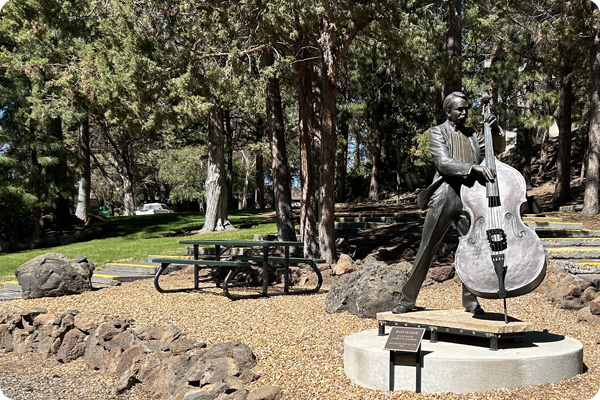 Picnic table outside Pence Hall in front of a statue playing an upright bass.