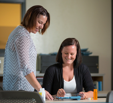 Two people working together at a table with medication bottles.
