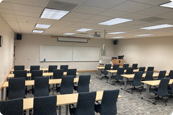 Classroom with 4 rows of desk and chairs. video conferencing camera hangs from the ceiling.