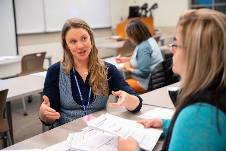 Instructor has an animated conversation with a student in a classroom