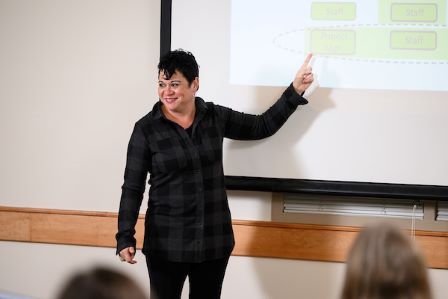 Project Management Instructor teaching in front of class pointing to presentation on screen