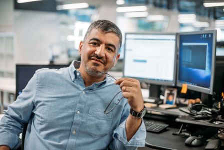 Man smiling while facing away from his computer holding his glasses