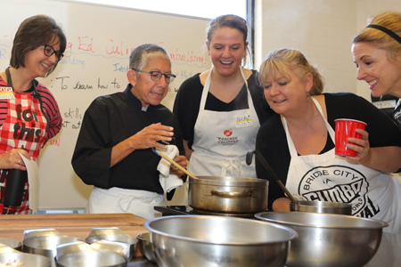 Four culinary students observe an instructor give directions while food cooks in a pot