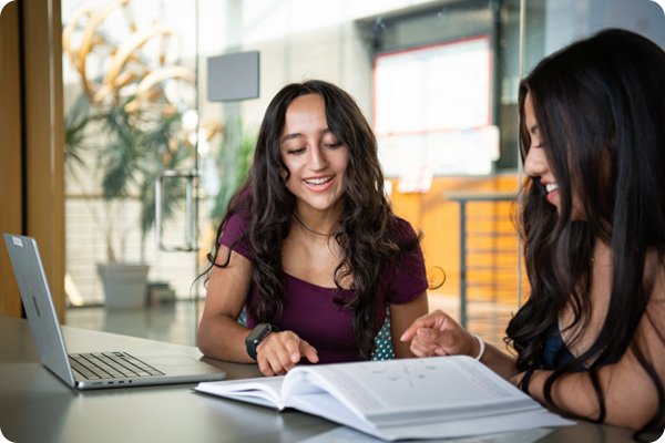 Two women studying together with a book and a laptop