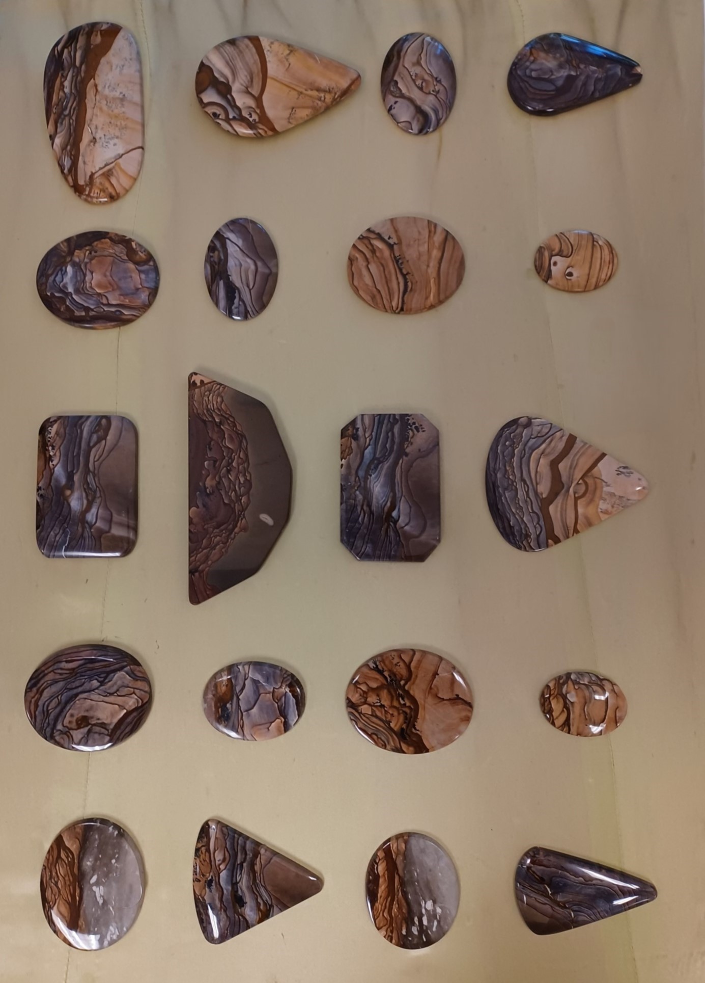 Polished jasper in a variety of shapes, showing striated colors in shades of of beige, gray, black, brown, and white. 
