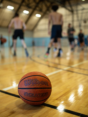 Close-up shot of a Basketball on the gym floor while players runs around in the background