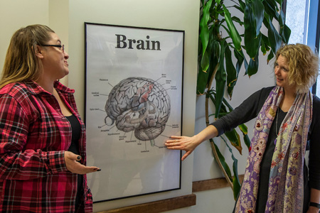 Professor pointing to a graphic image depicting different parts of the human brain to a student