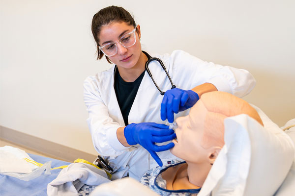 BSN nursing student wearing gloves practices patient care skills on a medical simulation mannequin.