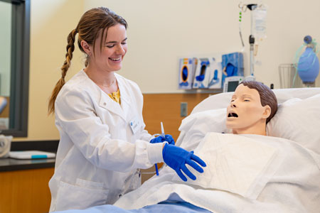 Nursing student practices clinical skills on a medical simulation mannequin in a nursing lab.