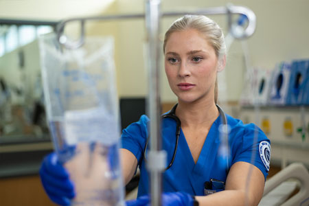 Nursing student adjusts an IV bag while providing patient care in a simulated hospital setting.