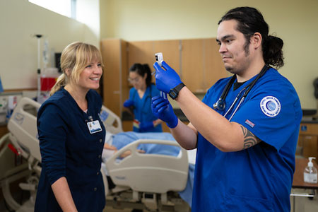 Nursing student prepares medication under instructor supervision during hands-on clinical training.